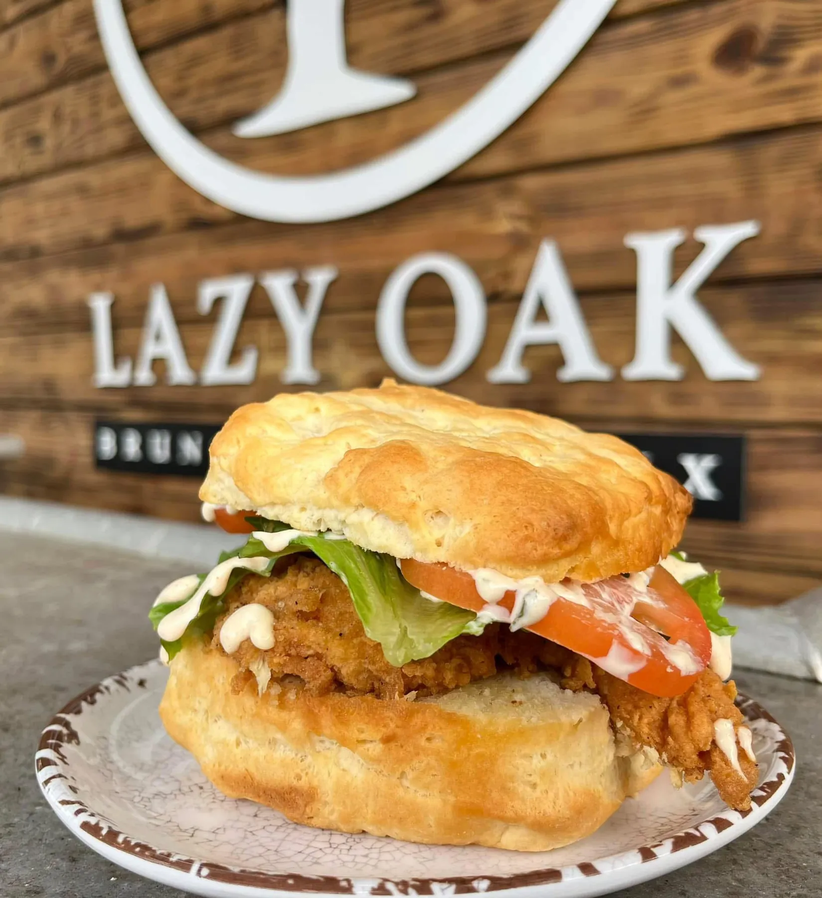 Fried chicken biscuit in front of the Lazy Oak sign